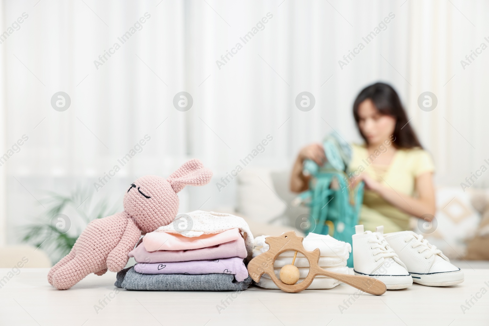 Photo of Baby's stuff on white table and mother packing bag, selective focus