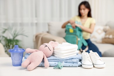 Photo of Baby's stuff on white table and mother packing bag, selective focus