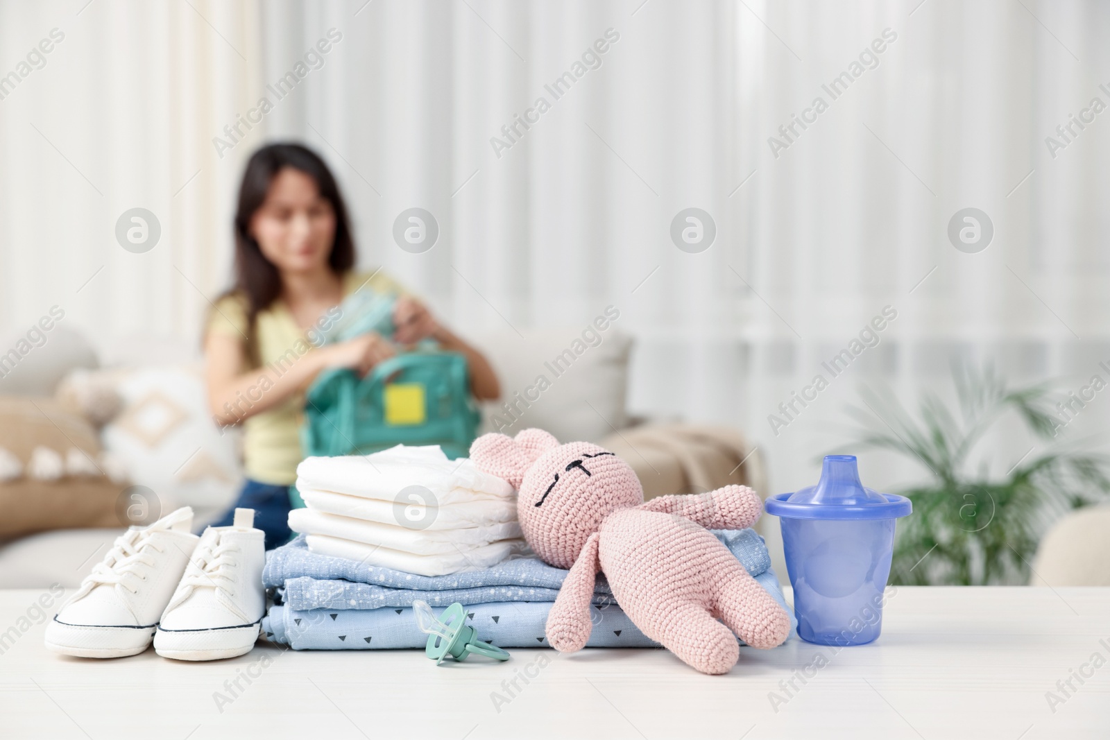 Photo of Baby's stuff on white table and mother packing bag, selective focus