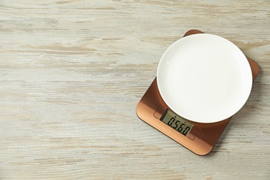 Photo of Modern electronic kitchen scale with plate on wooden table, top view. Space for text