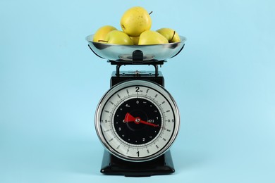 Photo of Mechanical kitchen scale with bowl of apples on light blue background