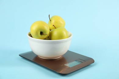 Photo of Electronic kitchen scale with bowl of apples on light blue background, closeup