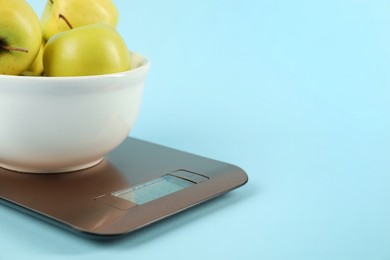 Photo of Electronic kitchen scale with bowl of apples on light blue background, closeup. Space for text