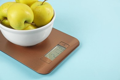 Photo of Electronic kitchen scale with bowl of apples on light blue background, closeup. Space for text