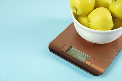 Photo of Electronic kitchen scale with bowl of apples on light blue background, closeup. Space for text