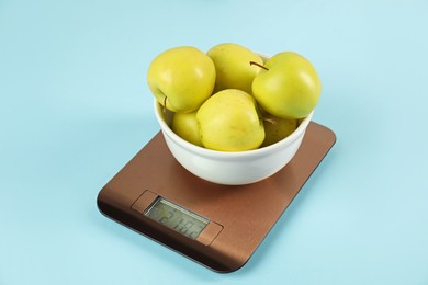 Photo of Electronic kitchen scale with bowl of apples on light blue background, closeup