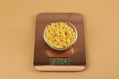 Photo of Electronic kitchen scale with bowl of raw pasta on beige background