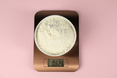 Photo of Electronic kitchen scale with bowl of flour on pink background, top view