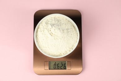 Photo of Electronic kitchen scale with bowl of flour on pink background, top view