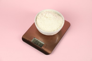 Photo of Electronic kitchen scale with bowl of flour on pink background