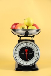 Photo of Mechanical kitchen scale with bowl of apples on yellow background