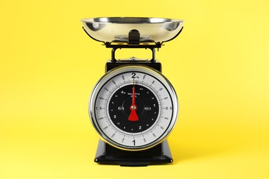 Photo of Mechanical kitchen scale with bowl on yellow background, closeup