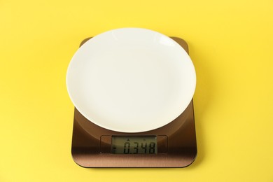 Photo of Electronic kitchen scale with empty plate on yellow background, closeup