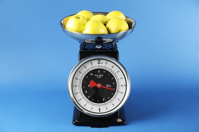 Photo of Mechanical kitchen scale with bowl of apples on blue background