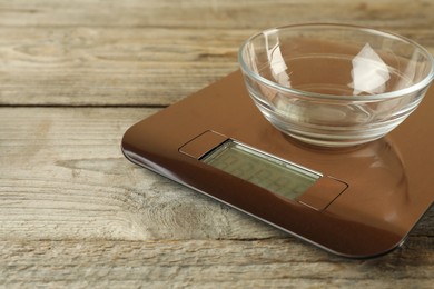 Photo of Electronic kitchen scale with empty bowl on wooden table, closeup. Space for text