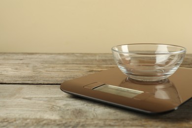 Photo of Electronic kitchen scale with empty bowl on wooden table against beige background, closeup. Space for text