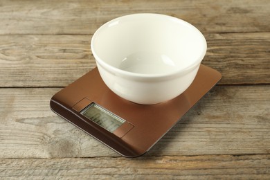 Photo of Electronic kitchen scale with empty bowl on wooden table, closeup