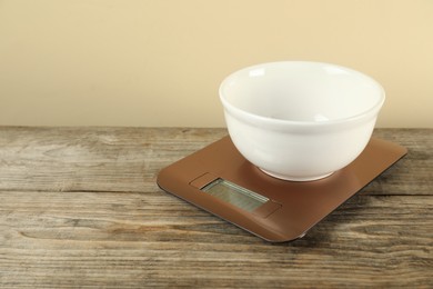 Photo of Electronic kitchen scale with empty bowl on wooden table against beige background. Space for text