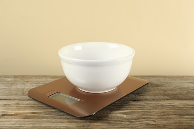 Photo of Electronic kitchen scale with empty bowl on wooden table against beige background, closeup