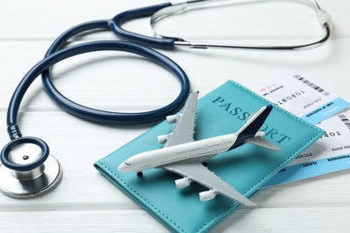 Photo of Medical tourism. Stethoscope, plane model, passport and flight tickets on white wooden table, closeup