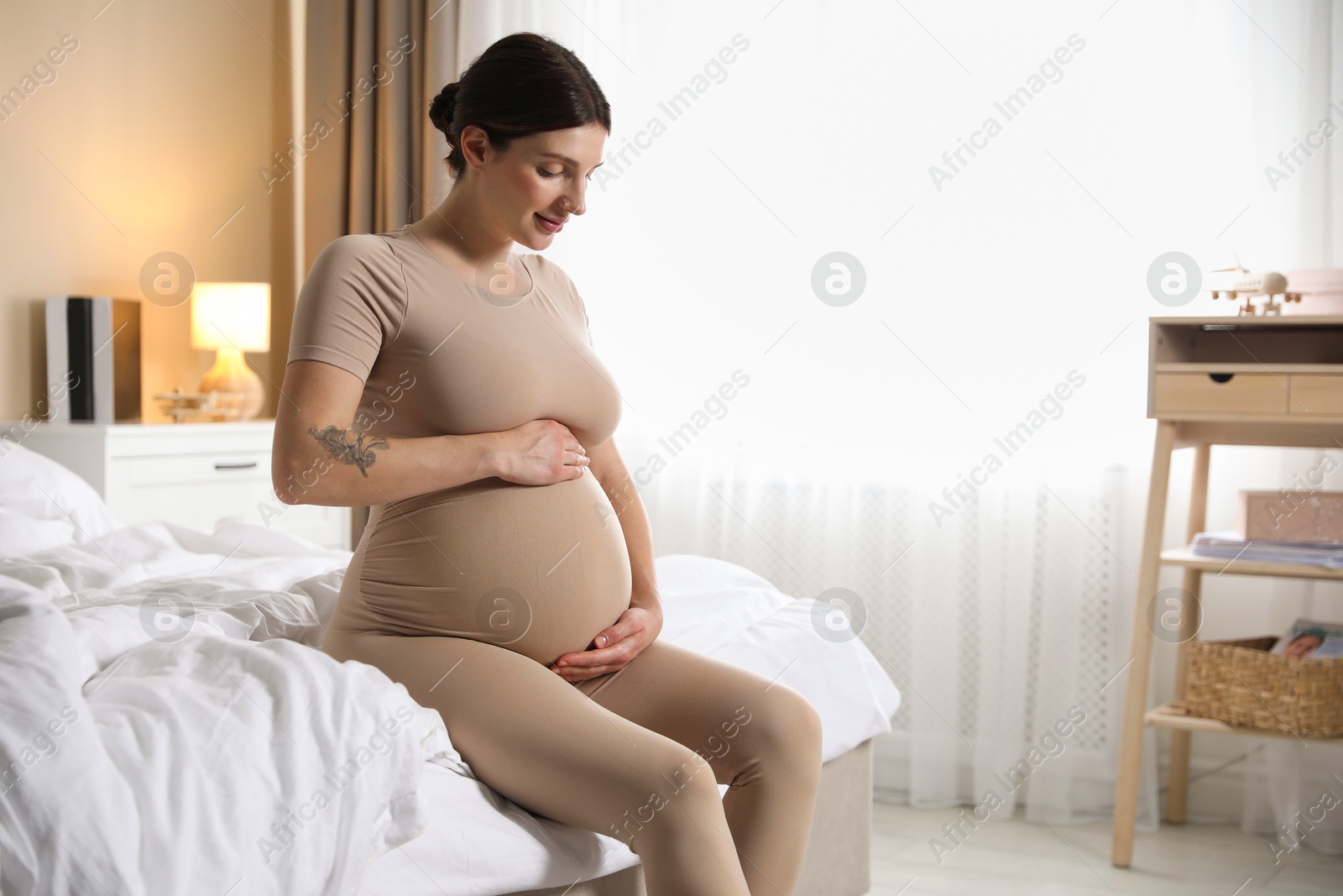 Photo of Beautiful pregnant woman on bed at home. Space for text