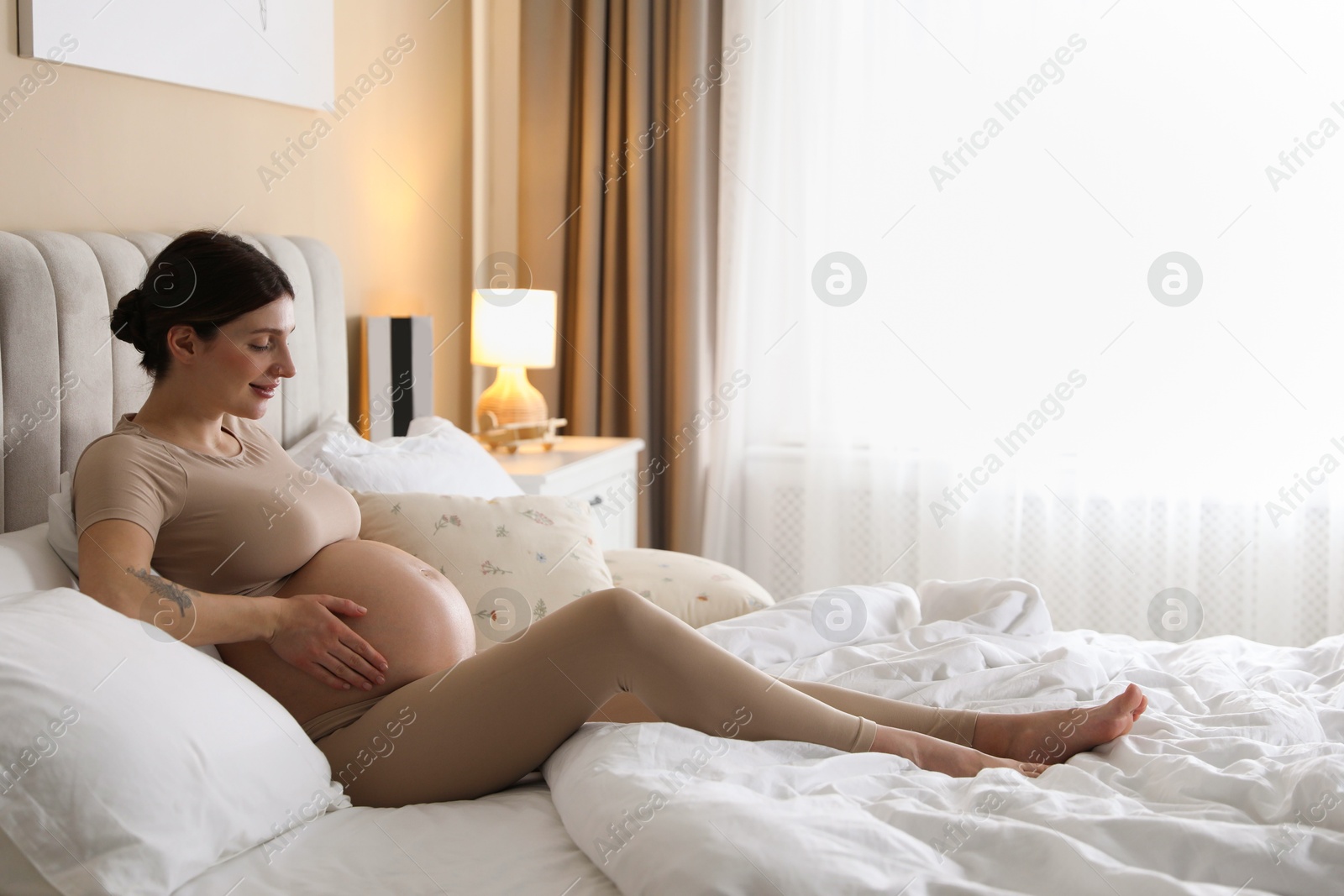 Photo of Beautiful pregnant woman on bed at home. Space for text