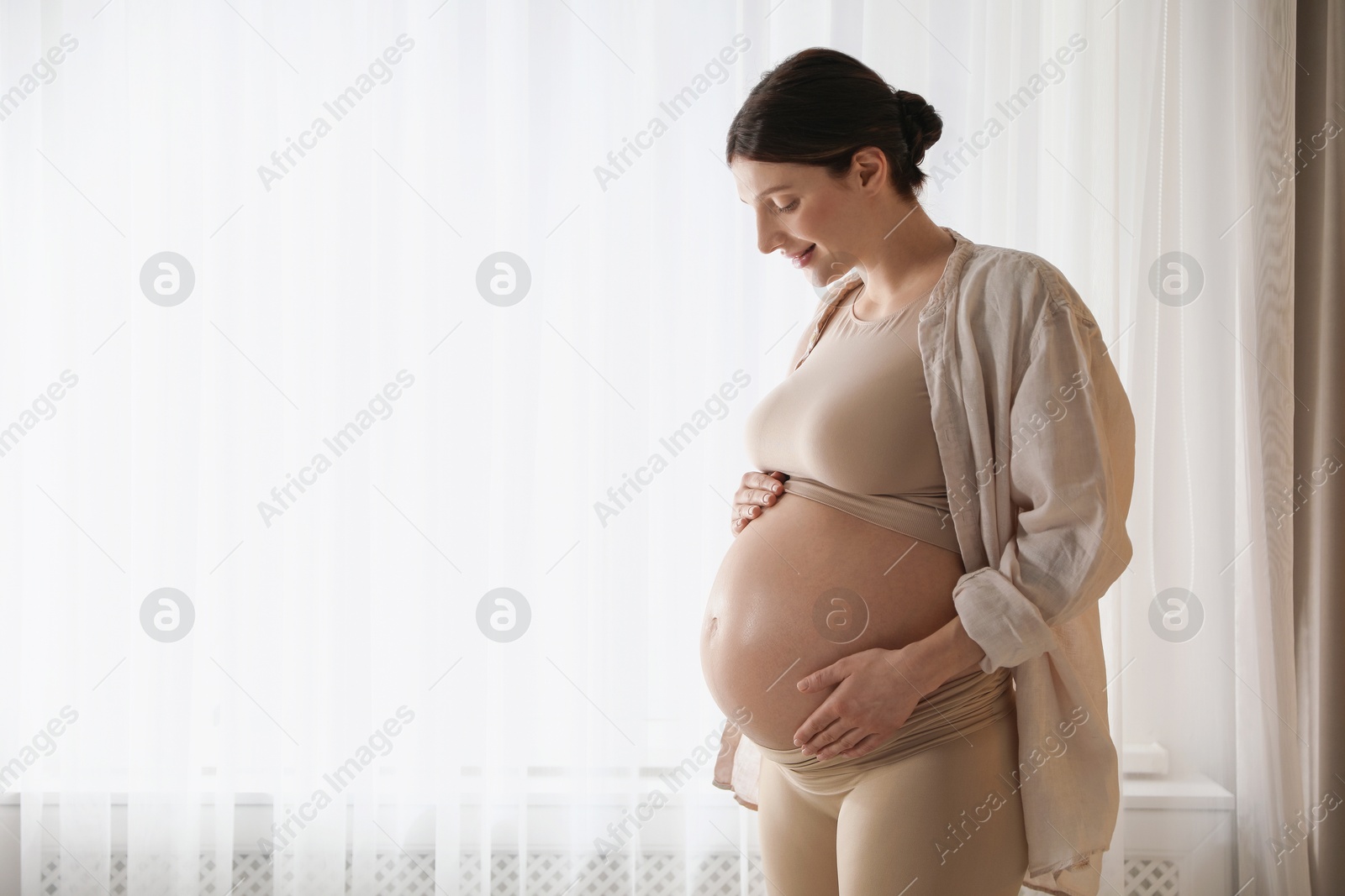 Photo of Beautiful pregnant woman near window at home. Space for text