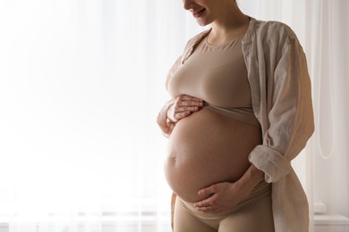 Pregnant woman near window at home, closeup. Space for text