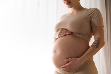 Pregnant woman near window at home, closeup. Space for text