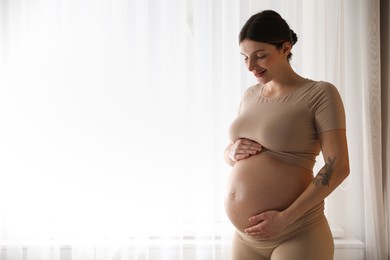 Beautiful pregnant woman near window at home. Space for text