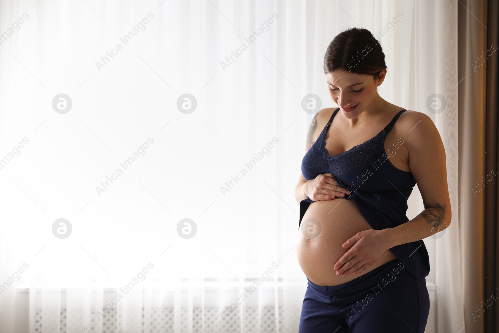 Photo of Beautiful pregnant woman near window at home. Space for text