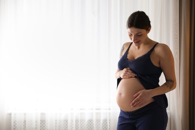 Beautiful pregnant woman near window at home. Space for text