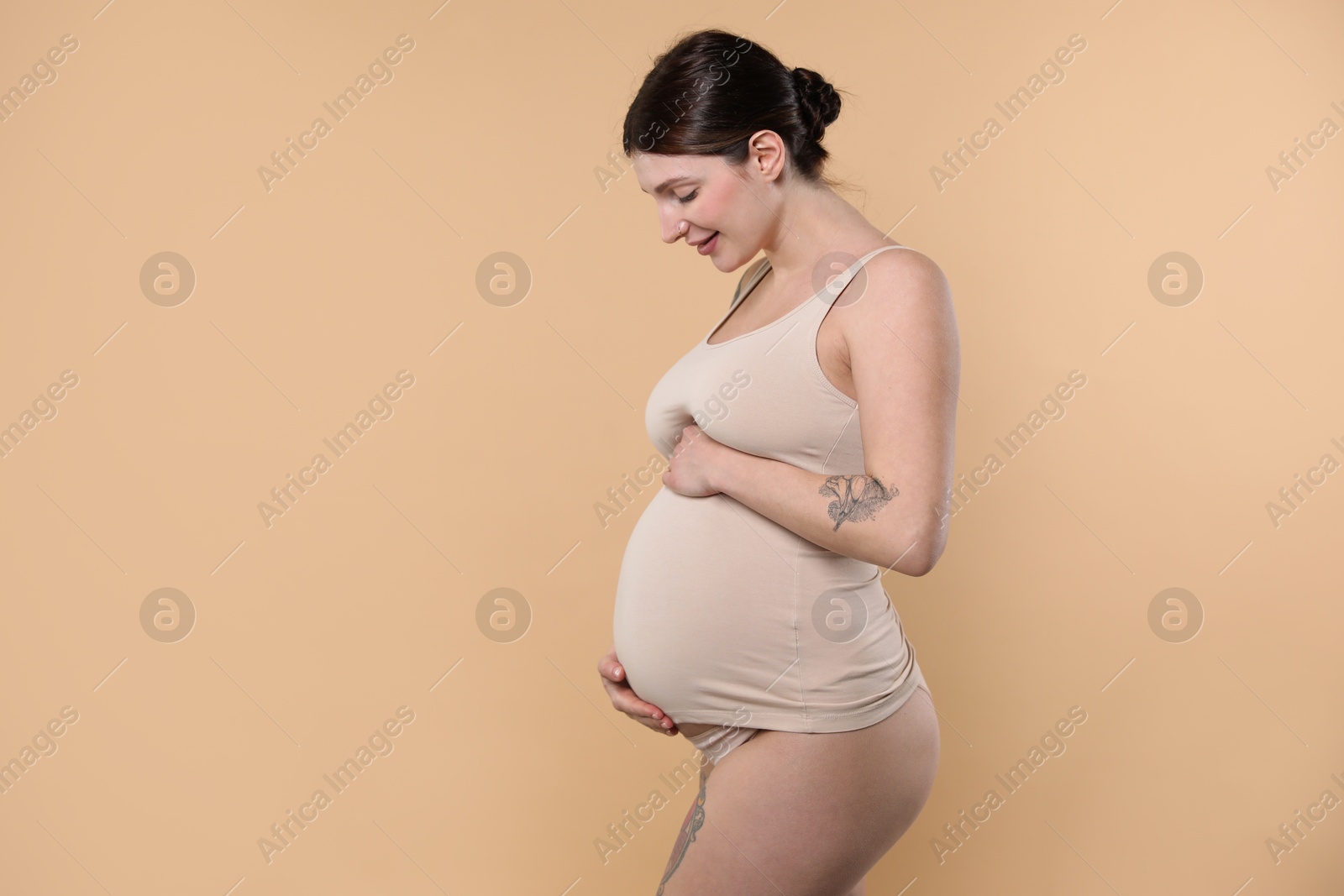 Photo of Beautiful pregnant woman with cute belly on beige background. Space for text