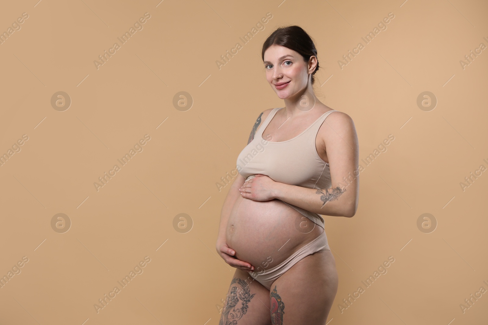 Photo of Beautiful pregnant woman with cute belly on beige background. Space for text