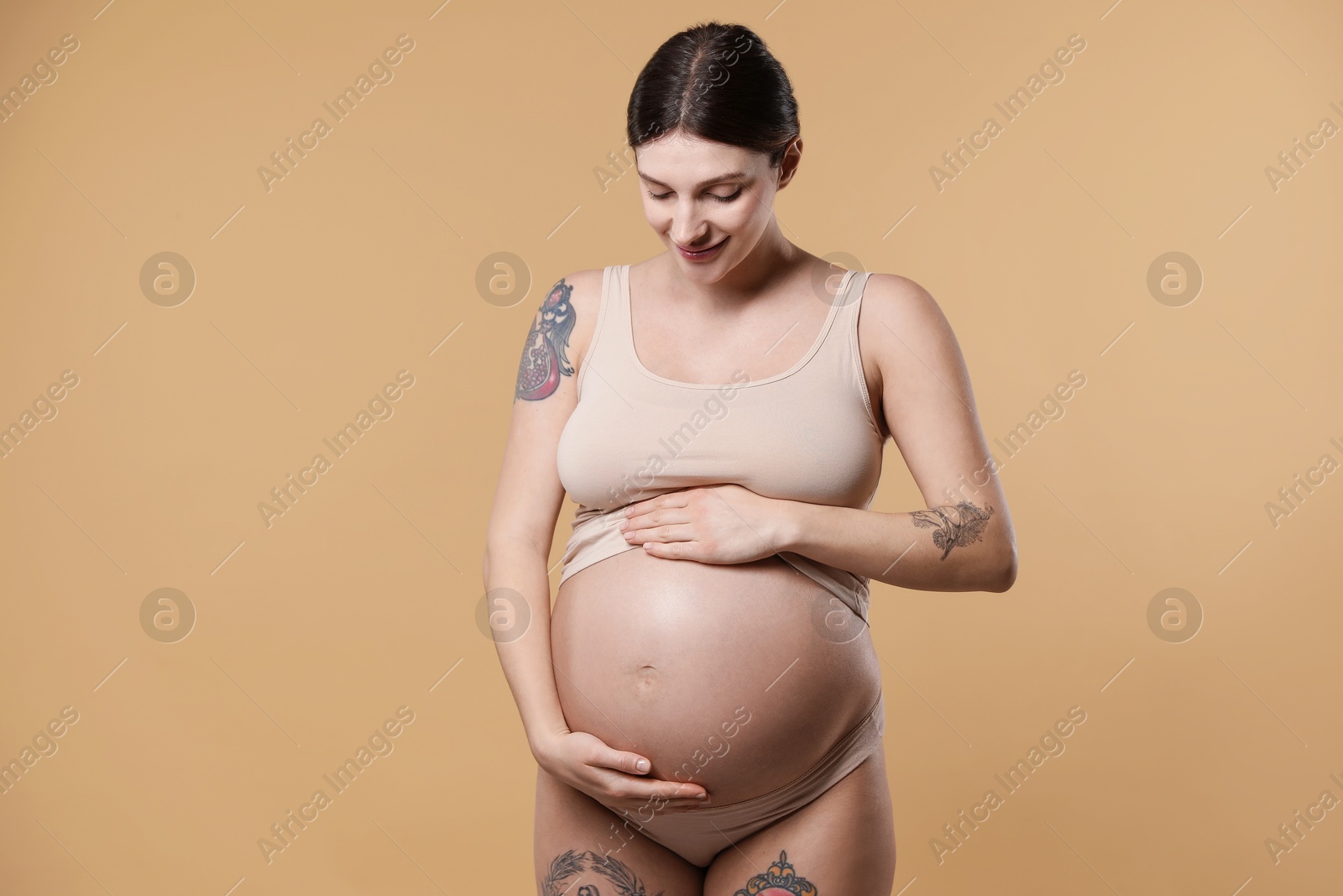 Photo of Beautiful pregnant woman with cute belly on beige background