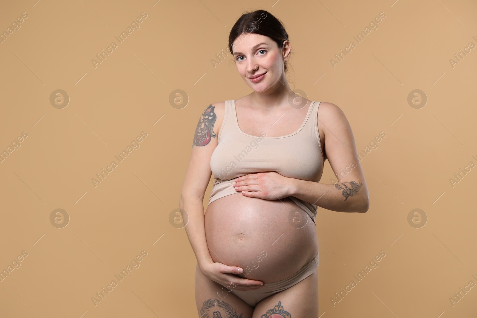 Photo of Beautiful pregnant woman with cute belly on beige background