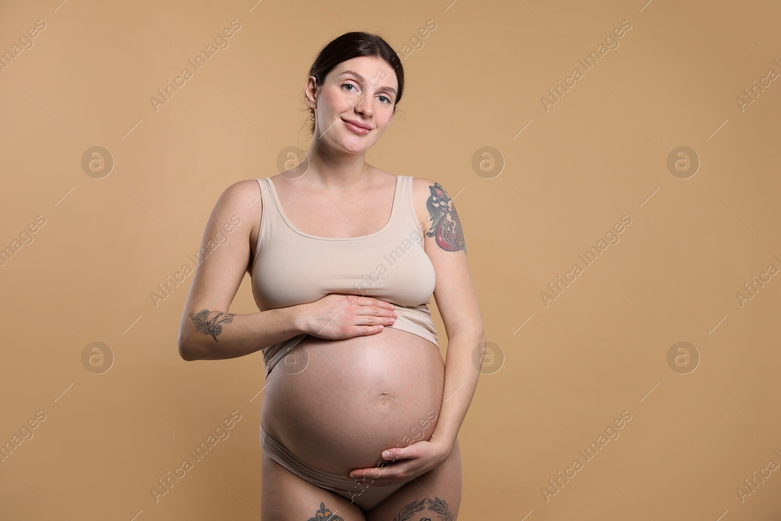 Photo of Beautiful pregnant woman with cute belly on beige background