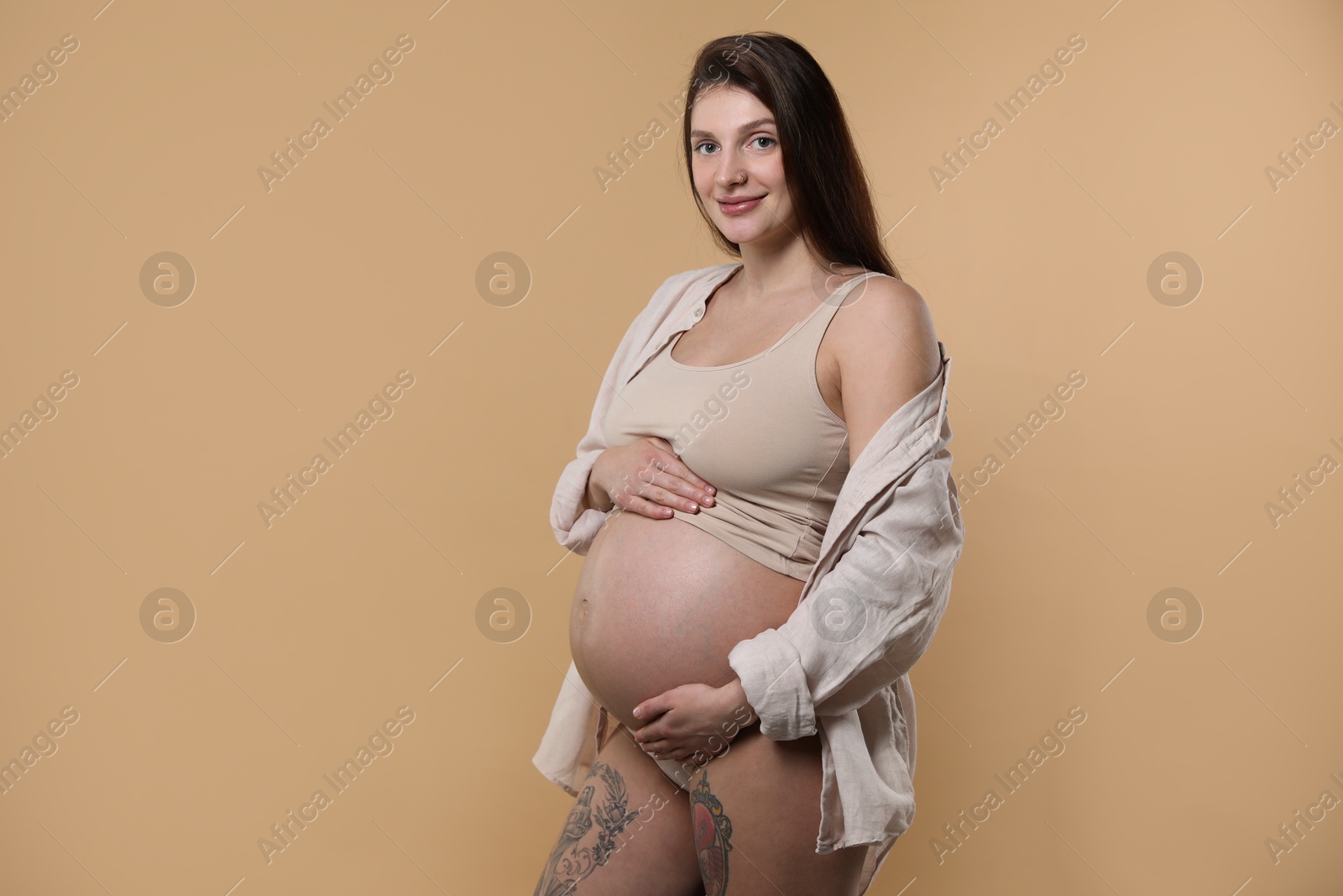 Photo of Beautiful pregnant woman with cute belly on beige background. Space for text