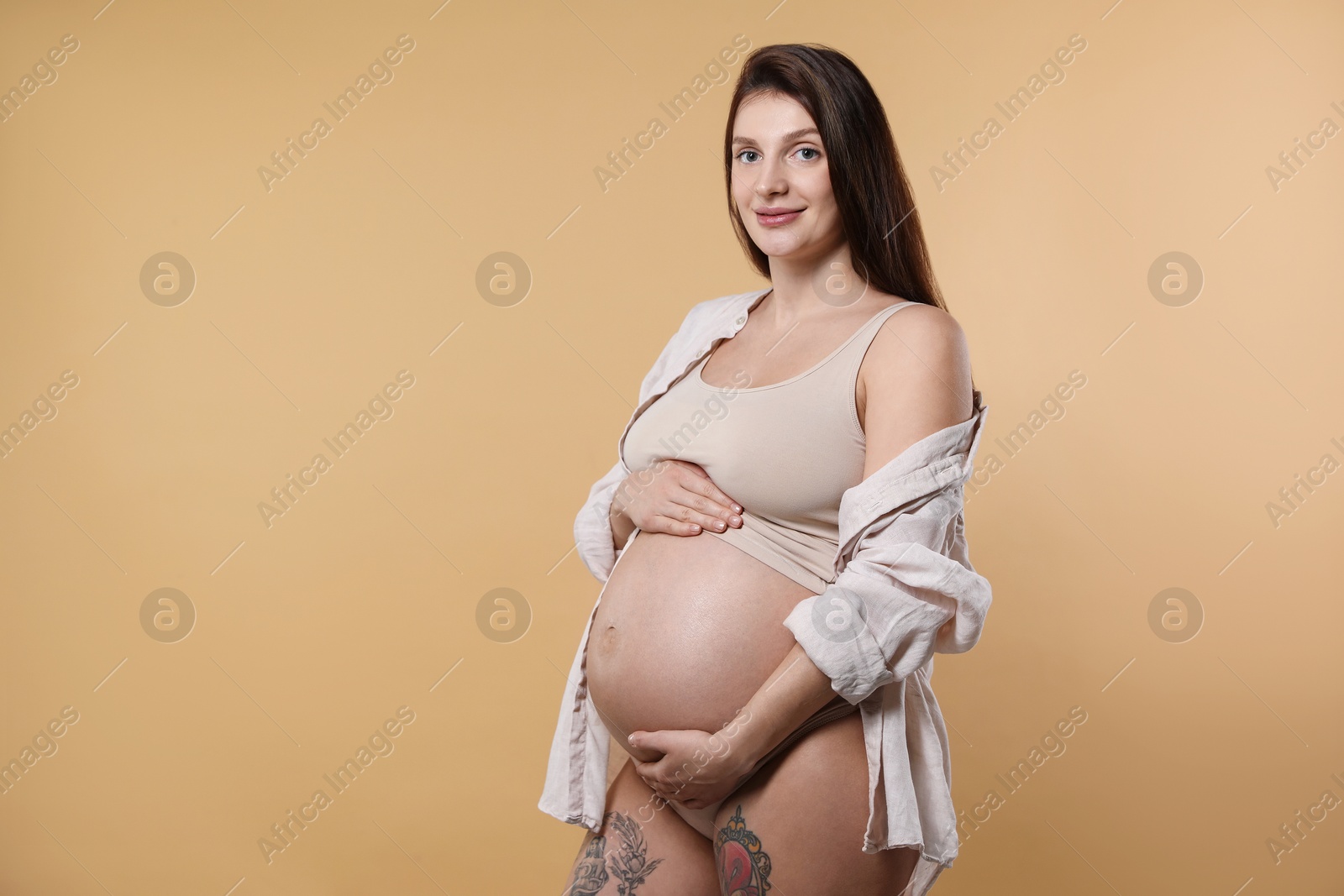 Photo of Beautiful pregnant woman with cute belly on beige background. Space for text