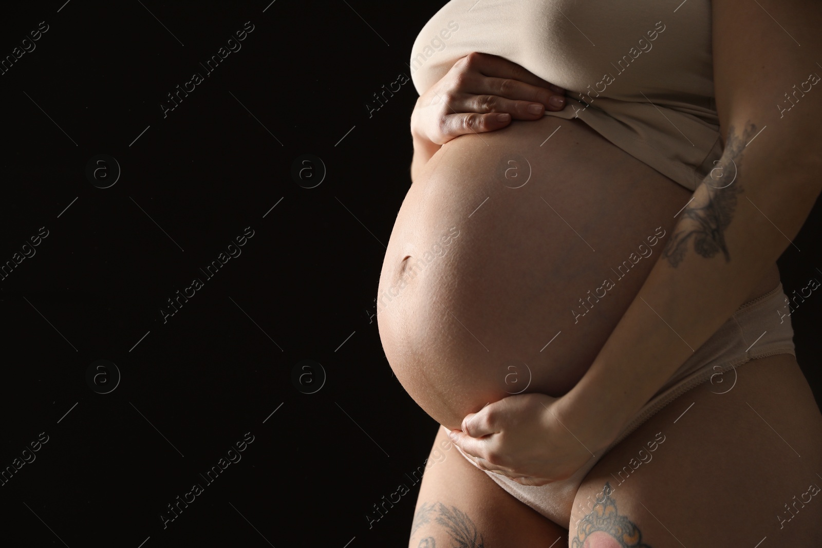 Photo of Pregnant woman with cute belly on black background, closeup. Space for text