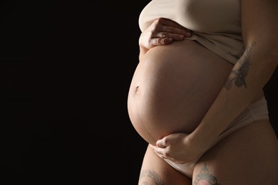 Pregnant woman with cute belly on black background, closeup. Space for text