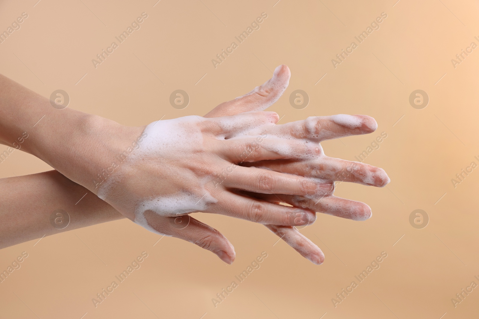 Photo of Woman washing hands with foaming soap on beige background, closeup. Hygiene