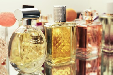 Photo of Different aromatic perfumes in bottles on mirror surface, closeup