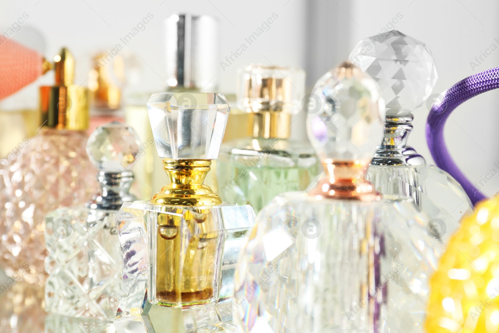 Photo of Different aromatic perfumes in bottles on mirror surface, closeup