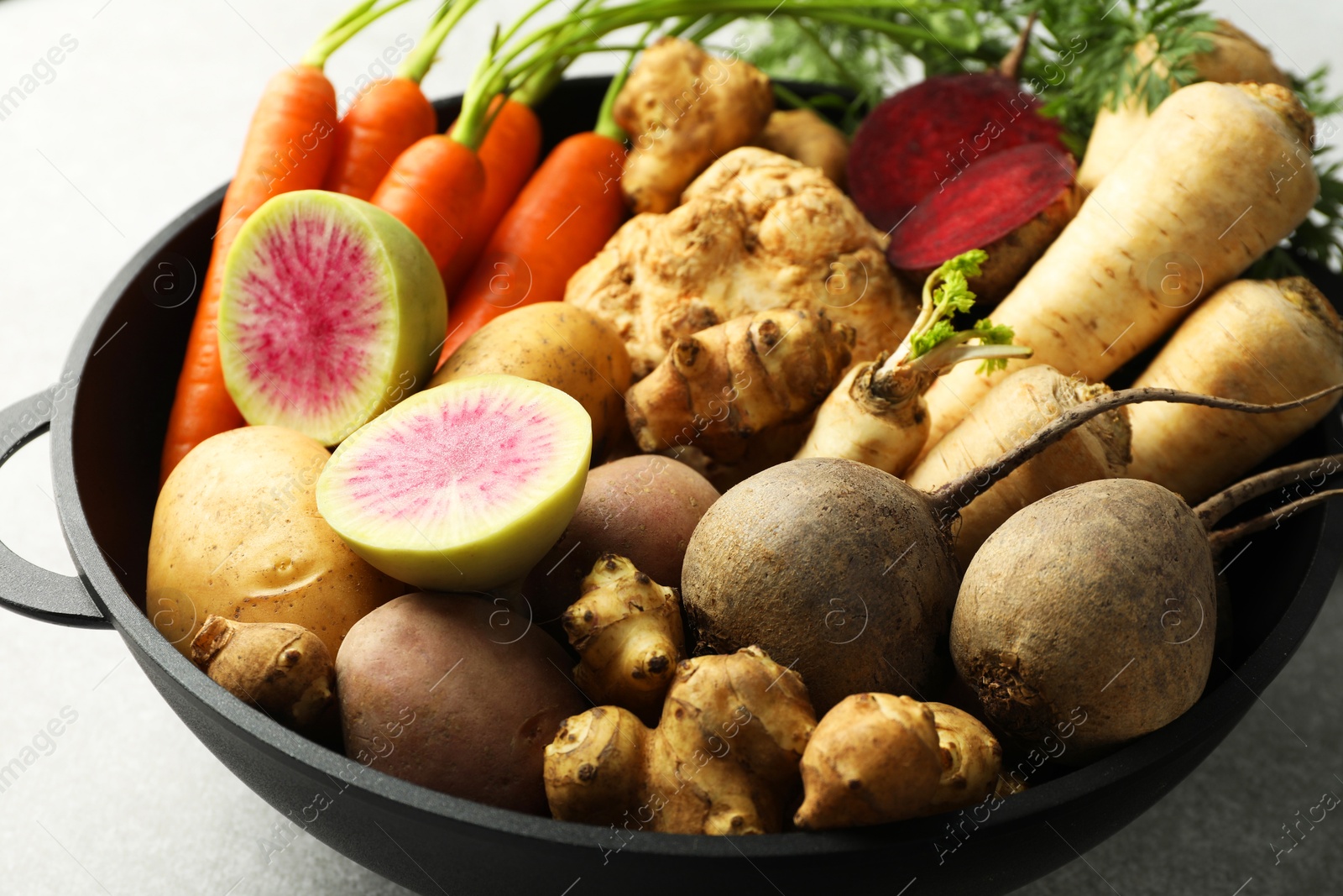 Photo of Different root vegetables in pot on light grey table, closeup