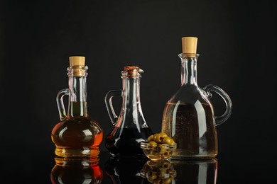 Photo of Salad dressings and olives on mirror surface against black background