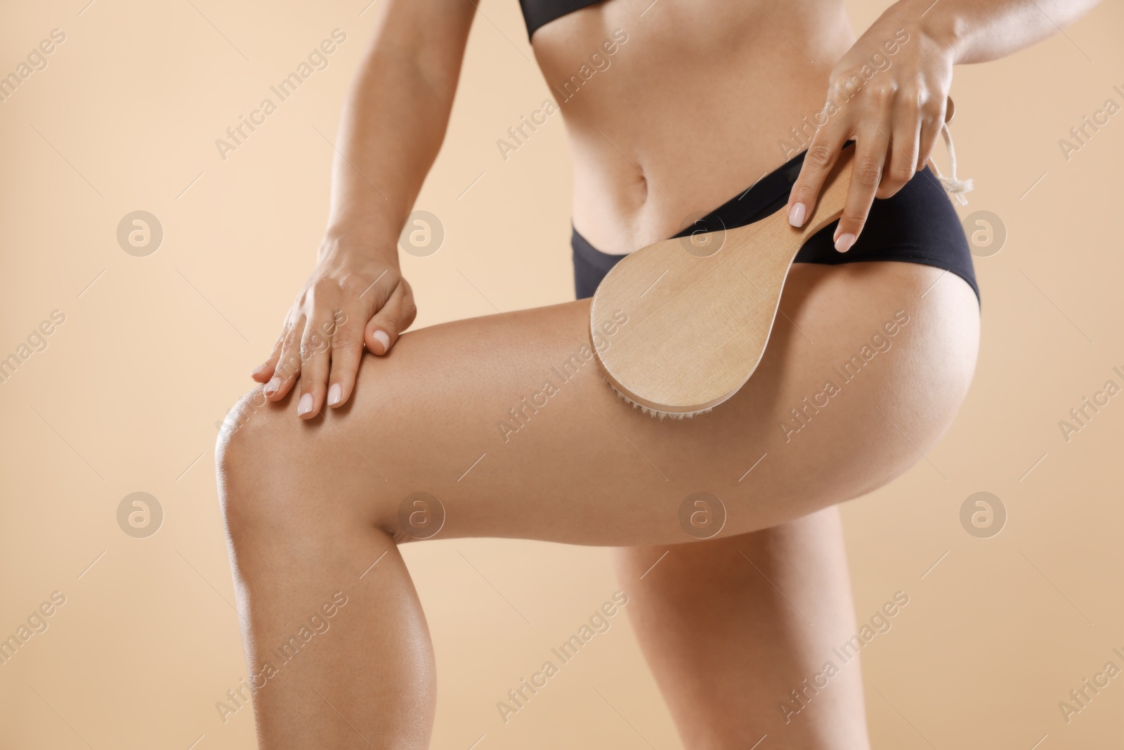 Photo of Woman doing anti cellulite massage with brush on beige background, closeup