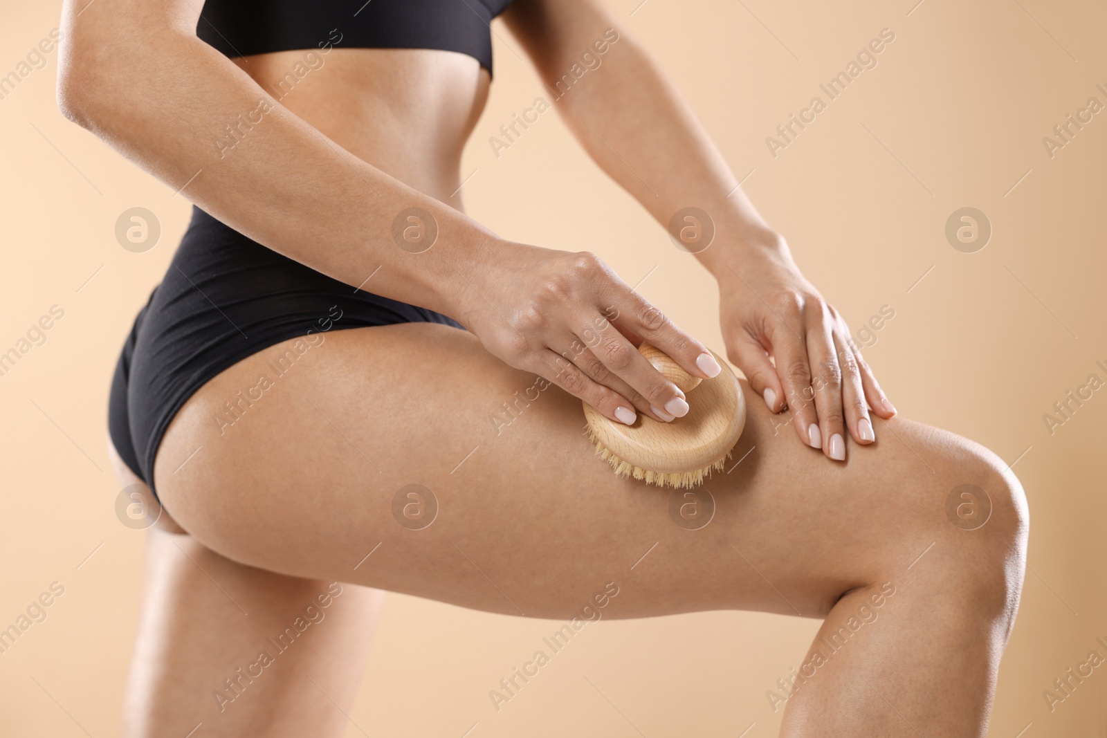 Photo of Woman doing anti cellulite massage with brush on beige background, closeup