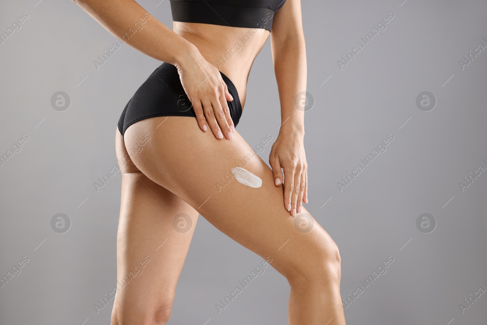 Photo of Woman applying anti cellulite cream on grey background, closeup