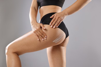 Woman applying anti cellulite cream on grey background, closeup